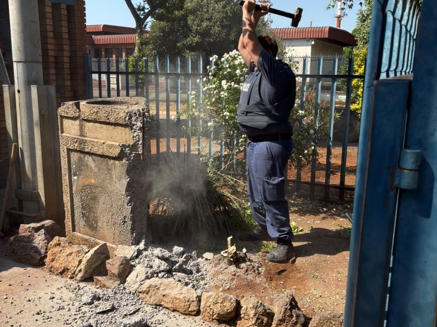 Uniformed police officer swinging a sledgehammer at an old concrete structure at the station entrance